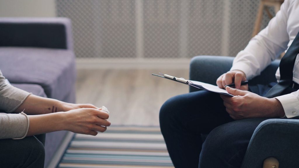 A therapy session with a psychologist and patient, discussing mental health indoors.